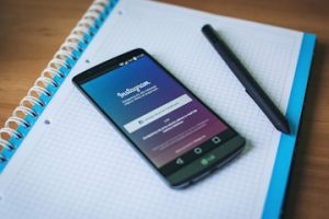 Miniatura, sobre una libreta de anillas con papel cuadriculado y bordes azules, vemos un móvil que muestra la aplicación Instagram junto a un lápiz digital